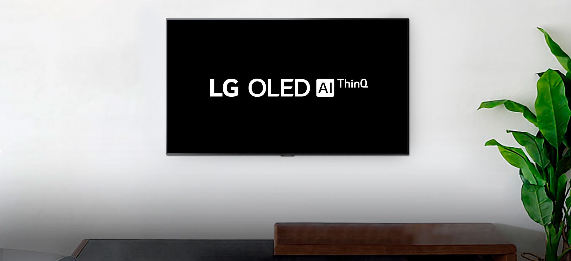 Zamontowany na ścianie telewizor z wyświetlonym logo LG OLED AI ThinQ na czarnym tle