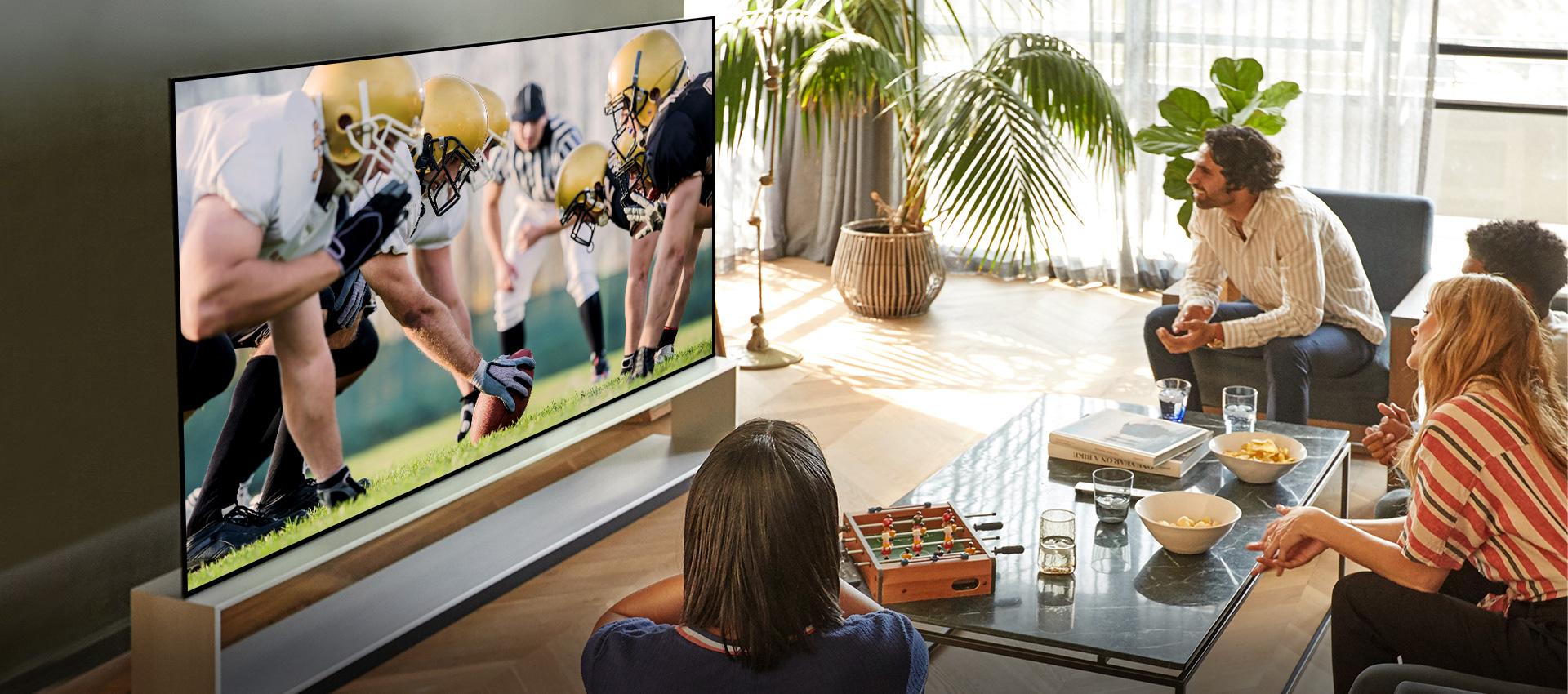 Grupa znajomych w salonie ogląda mecz piłki nożnej na telewizorze o szerokim kącie widzenia