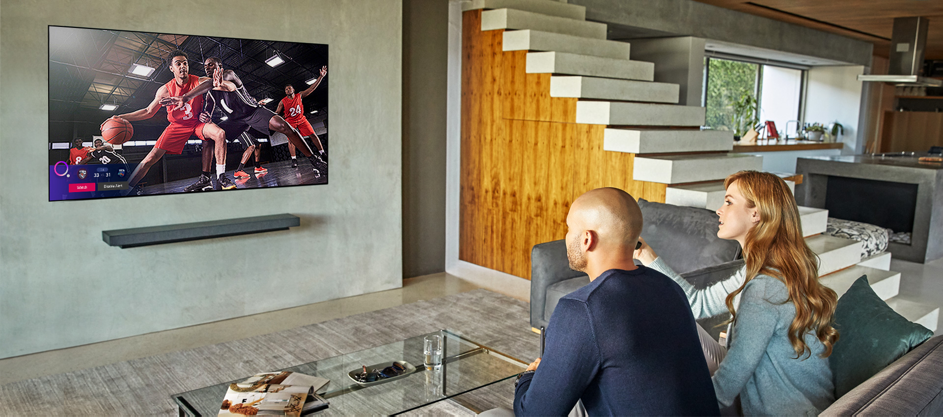 Para oglądająca mecz koszykówki, a w lewym dolnym rogu ekranu wyświetlony jest alarm informujący o wynikach innych meczów
