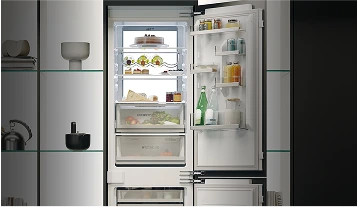 Otwarta lodówka w nowoczesnej kuchni, z dobrze zorganizowanymi półkami pełnymi owoców, warzyw, ciast i napojów, w minimalistycznym otoczeniu.