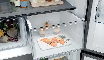 Otwarta lodówka z dobrze zorganizowanymi półkami, zawierająca słoiki z pomarańczowymi i żółtymi zawartościami, białe sery, zielone warzywa oraz talerz z filetem łososia ozdobionym koperkiem i plasterkami cytryny.