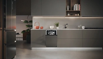 Nowoczesna kuchnia z szarymi szafkami, stalowymi urządzeniami i minimalistycznym wystrojem. Widoczna wbudowana zmywarka z otwartymi drzwiami. Kuchnia charakteryzuje się prostymi liniami i ciepłym oświetleniem.