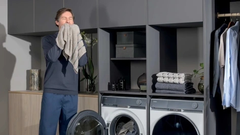 Mężczyzna w pralni wdycha zapach świeżo wypranych ręczników obok pralko–suszarek Haier