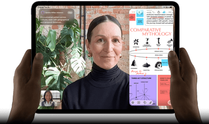 Widoczny od przodu ustawiony poziomo iPad Pro w kolorze gwiezdnej czerni, zaokrąglone rogi, czarna ramka wyświetlacza. Ręce trzymają urządzenie z lewej i prawej strony, na ekranie tłumaczona na żywo rozmowa przez FaceTime. Widać też aplikację edukacyjną z prezentacją „Comparative Mythology”, z tekstem, diagramami i odręcznymi notatkami