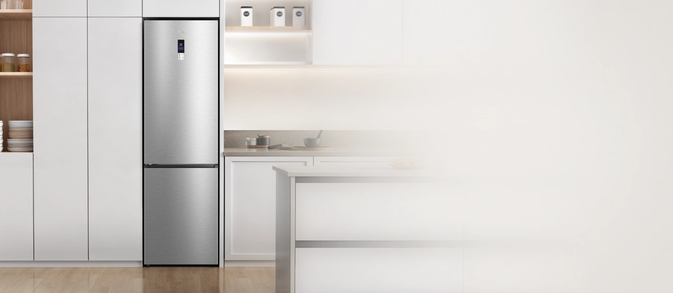 Srebrna lodówka wolnostojąca Tcl, z dolnym zamrażalnikiem, wkomponowana w minimalistyczną, białą kuchnię.