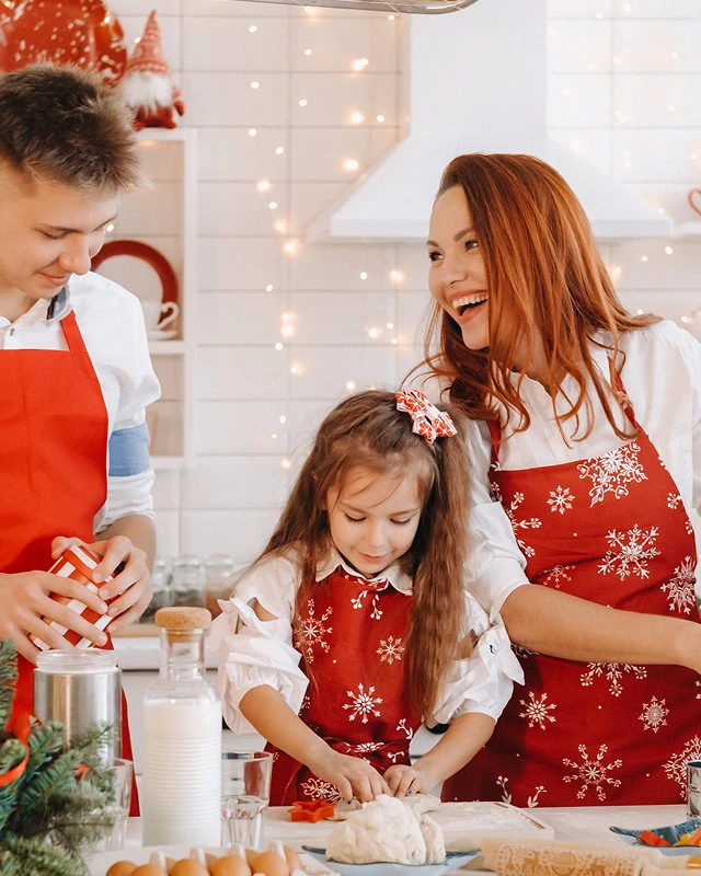 Czteroosobowa, uśmiechnięta rodzina w kuchni w czerwonych fartuchach przygotowuje świąteczne wypieki