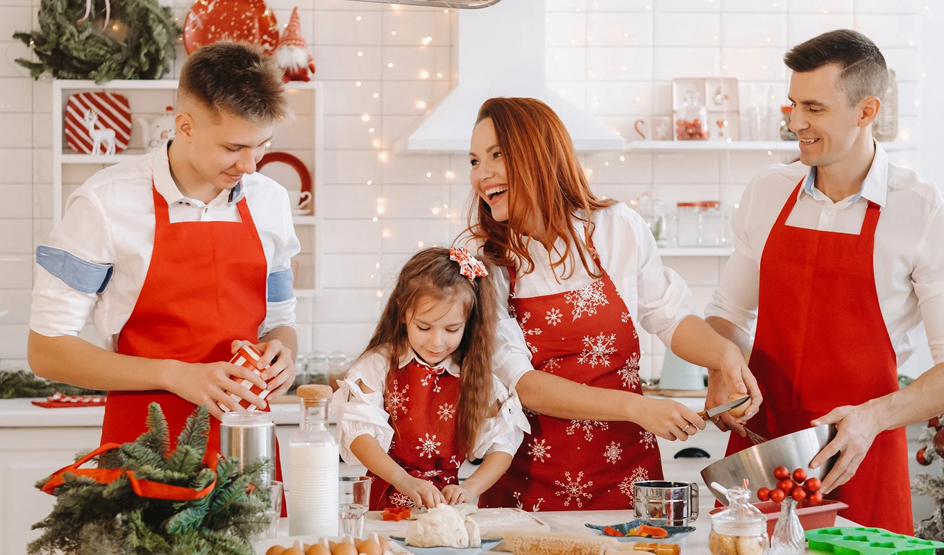 Czteroosobowa, uśmiechnięta rodzina w kuchni w czerwonych fartuchach przygotowuje świąteczne wypieki