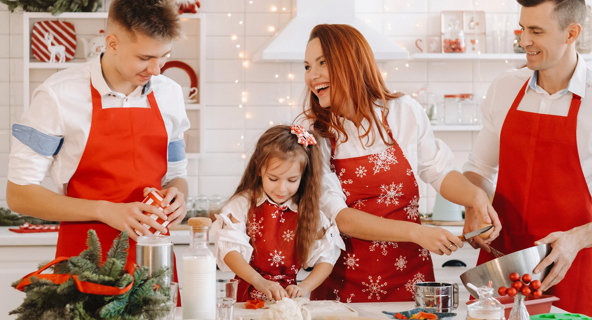 Czteroosobowa, uśmiechnięta rodzina w kuchni w czerwonych fartuchach przygotowuje świąteczne wypieki