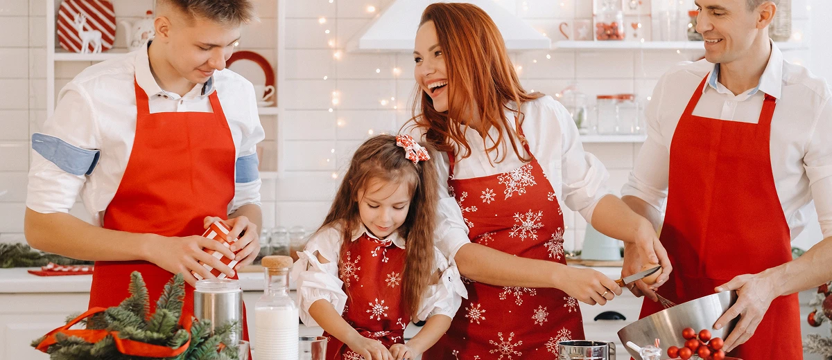 Czteroosobowa, uśmiechnięta rodzina w kuchni w czerwonych fartuchach przygotowuje świąteczne wypieki
