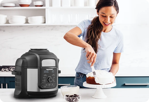 Kobieta nakłada białą polewę na ciasto, a obok na blacie leży Ninja Foodi Max OP500EU