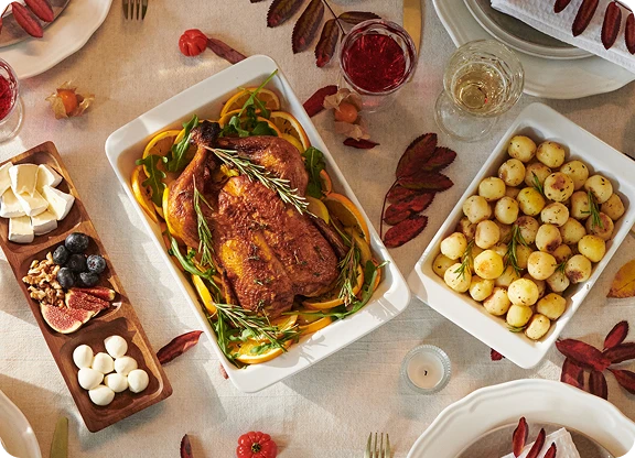 Widok od góry na potrawy świąteczne na udekorowanym stole, w tym na kurczaka w ziołach, ziemniaki, sery i owoce