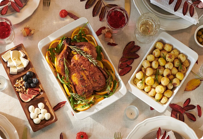 Widok od góry na potrawy świąteczne na udekorowanym stole, w tym na kurczaka w ziołach, ziemniaki, sery i owoce