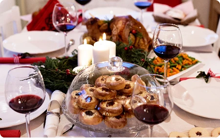 Zbliżenie na elegancko zastawiony stół świąteczny z białymi talerzami, potrawami świątecznymi, ciasteczkami i lampkami wina