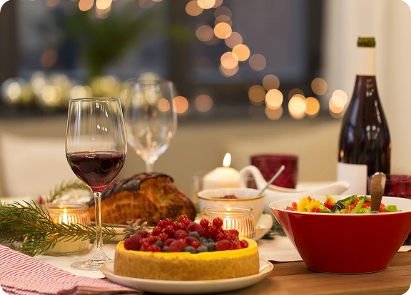 Zbliżenie na świąteczny stół, na którym jest ciasto z owocami i inne świąteczne potrawy oraz lampka wina