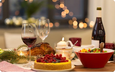 Zbliżenie na świąteczny stół, na którym jest ciasto z owocami i inne świąteczne potrawy oraz lampka wina