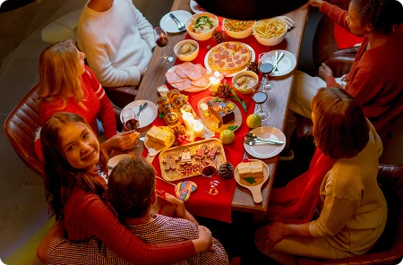 Widok od góry na uśmiechniętą dziewczynę siedzącą przy stole świątecznym w otoczeniu swoich bliskich