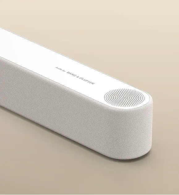 Zbliżenie na biały soundbar Bang & Olufsen z teksturowaną siatką głośnika i logo Audio by Bang & Olufsen