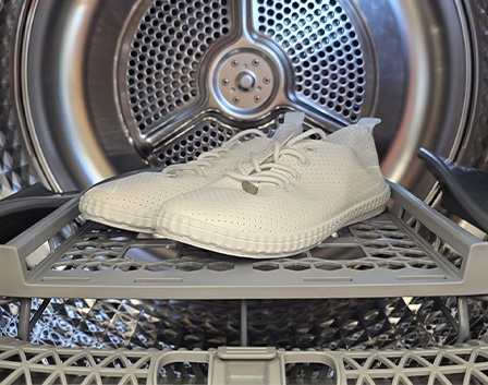 Białe buty wewnątrz suszarki bębnowej Samsung, pokazujące półkę do suszenia