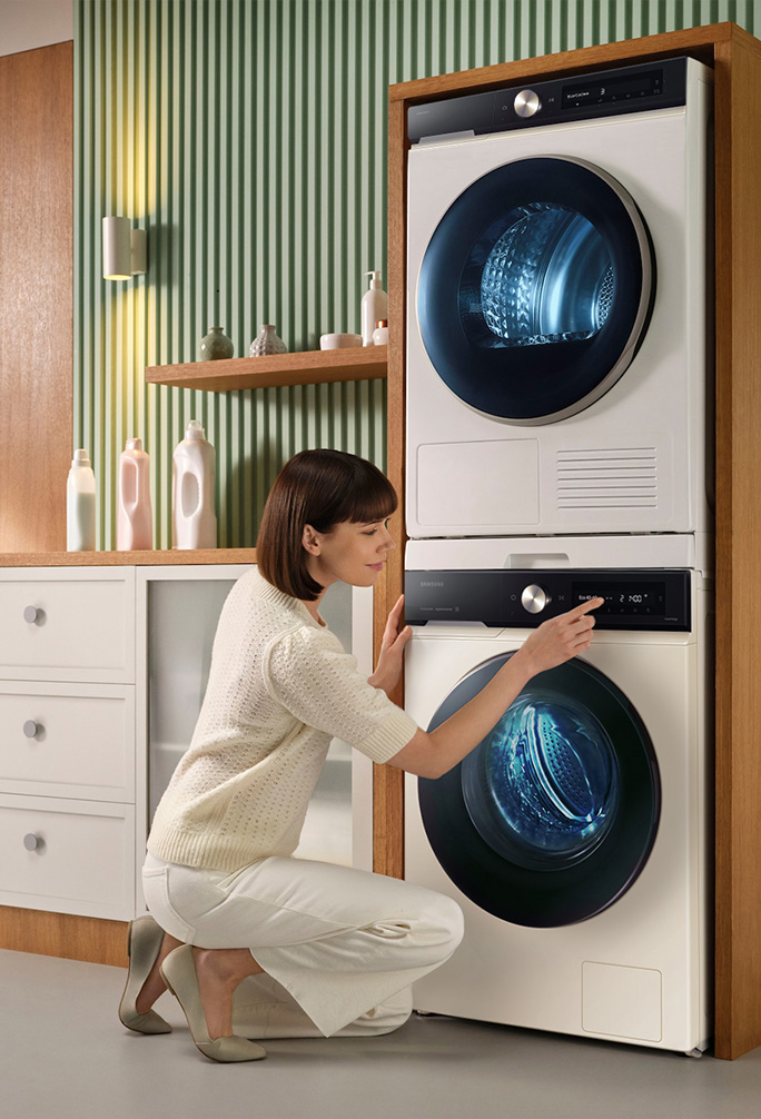 Osoba korzystająca z suszarki i kucająca przy jej drzwiach.