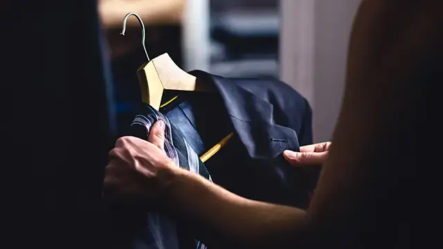 Czarny garnitur na wieszaku trzymany przez osobę w ciemnym pomieszczeniu.