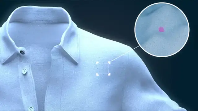 Biała koszula z różową plamą na ramieniu, powiększoną w okrągłym zbliżeniu.