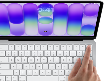 MacBook Neo w kolorze srebrnym z widocznym ekranem logowania i palcem osoby używającej czytnika Touch ID w prawym górnym rogu klawiatury