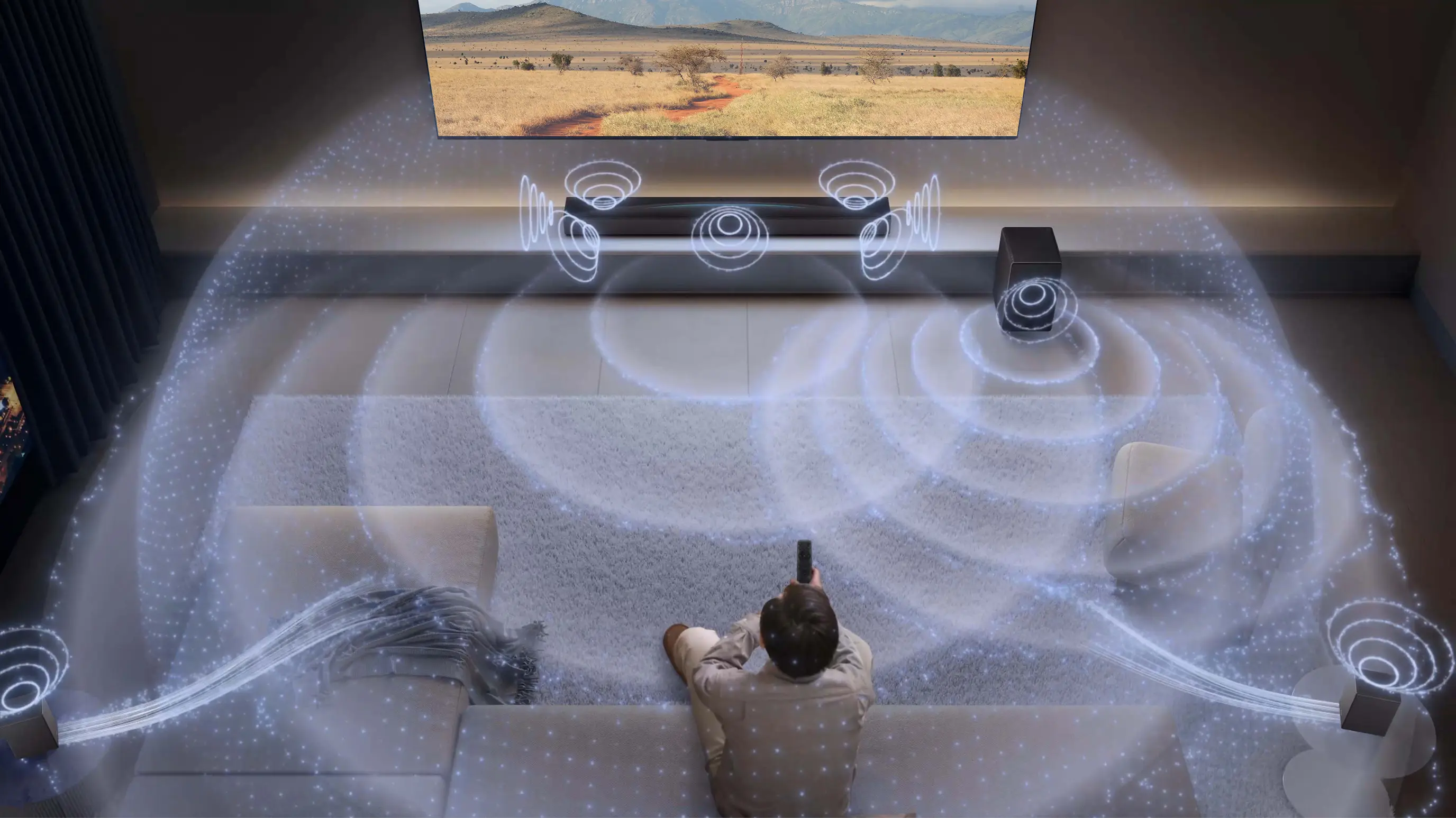 Widok salonu z góry w którym mężczyzna ogląda telewizje, soundbar Tcl i wizualizacja dźwięku 3D wypełniająca całą przestrzeń.