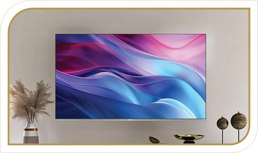 Telewizor Haier z kolorowym ekranem zamontowany na ścianie, obok dekoracje i wazon z trawą.