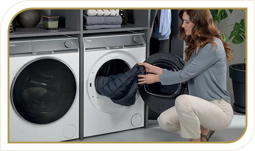 Suszarka Haier w zabudowie, otwierana przez kobietę wkładającą ciemną kurtkę. Obok ustawiona pralka Haier.
