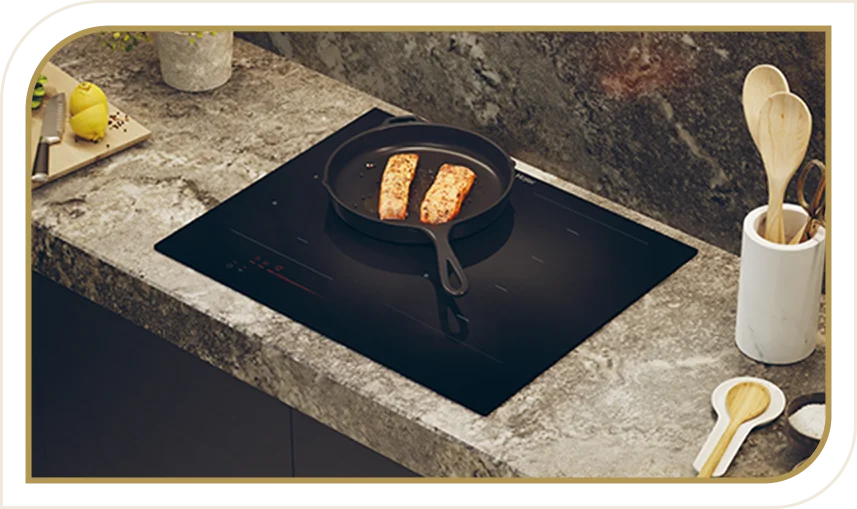 Czarna płyta indukcyjna zabudowana kamiennym blatem. Na płycie patelnia z dwoma kawałkami łososia.
