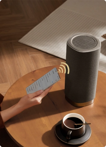 Osoba trzyma telefon blisko głośnika Tcl na stoliku, prezentując bezprzewodowe połączenie urządzeń