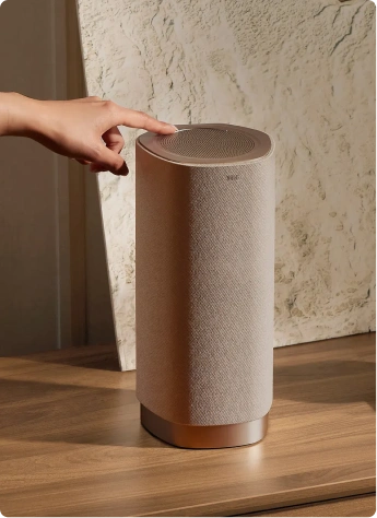 Dłoń dotyka górnej części eleganckiego głośnika Tcl ustawionego na drewnianym blacie