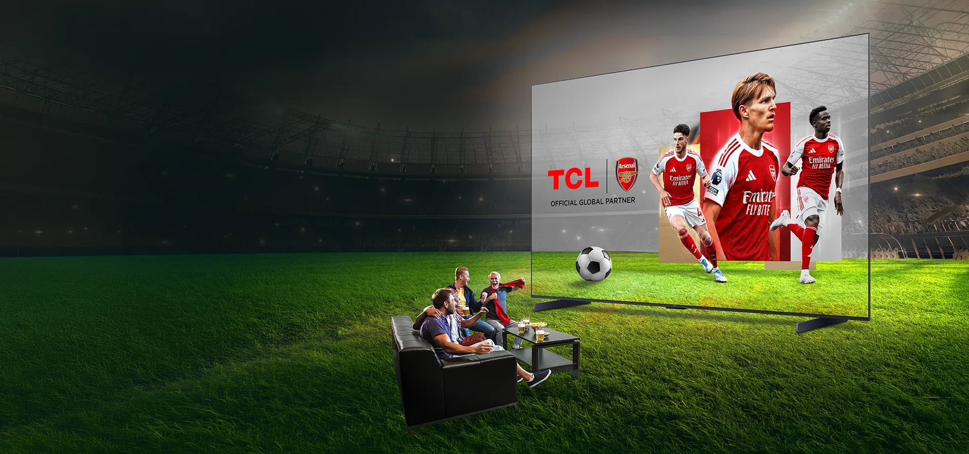 Telewizor Tcl z piłkarzami Arsenalu na ekranie, ustawiony na murawie stadionu z kibicami na sofie.