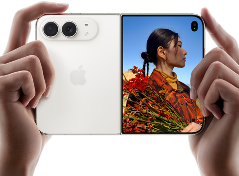 Trzymany w dwóch dłoniach rozłożony iPhone Duo w orientacji poziomej, lewy panel przedstawia aparaty tylne Fusion 48 MP, po prawej stronie na wyświetlaczu zewnętrznym widać osobę pozującą do zdjęcia, widzi ona swoją twarz podczas robienia zdjęcia dzięki funkcji Duo Preview