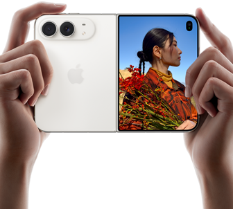 Trzymany w dwóch dłoniach rozłożony iPhone Duo w orientacji poziomej, lewy panel przedstawia aparaty tylne Fusion 48 MP, po prawej stronie na wyświetlaczu zewnętrznym widać osobę pozującą do zdjęcia, widzi ona swoją twarz podczas robienia zdjęcia dzięki funkcji Duo Preview