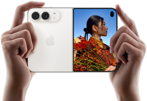 Trzymany w dwóch dłoniach rozłożony iPhone Duo w orientacji poziomej, lewy panel przedstawia aparaty tylne Fusion 48 MP, po prawej stronie na wyświetlaczu zewnętrznym widać osobę pozującą do zdjęcia, widzi ona swoją twarz podczas robienia zdjęcia dzięki funkcji Duo Preview