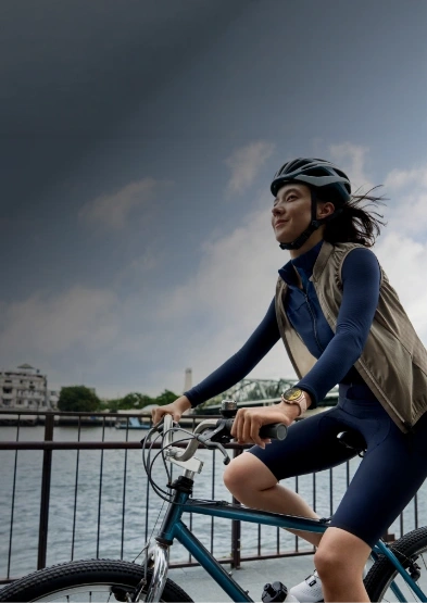 Zadowolona kobieta jedzie na miejskim rowerze promenadą nad wodą, na nadgarstku ma zegarek HUAWEI Watch 6 active różowy